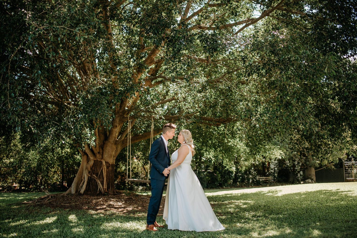 Newlyweds share an intimate moment on their wedding day in a sun-dappled garden setting.