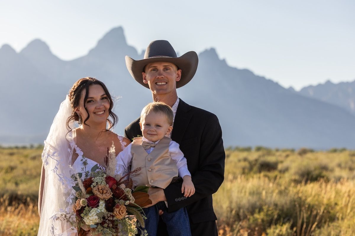 A couple in western wedding attire poses for romantic photos in a desert landscape with mountains in the background.