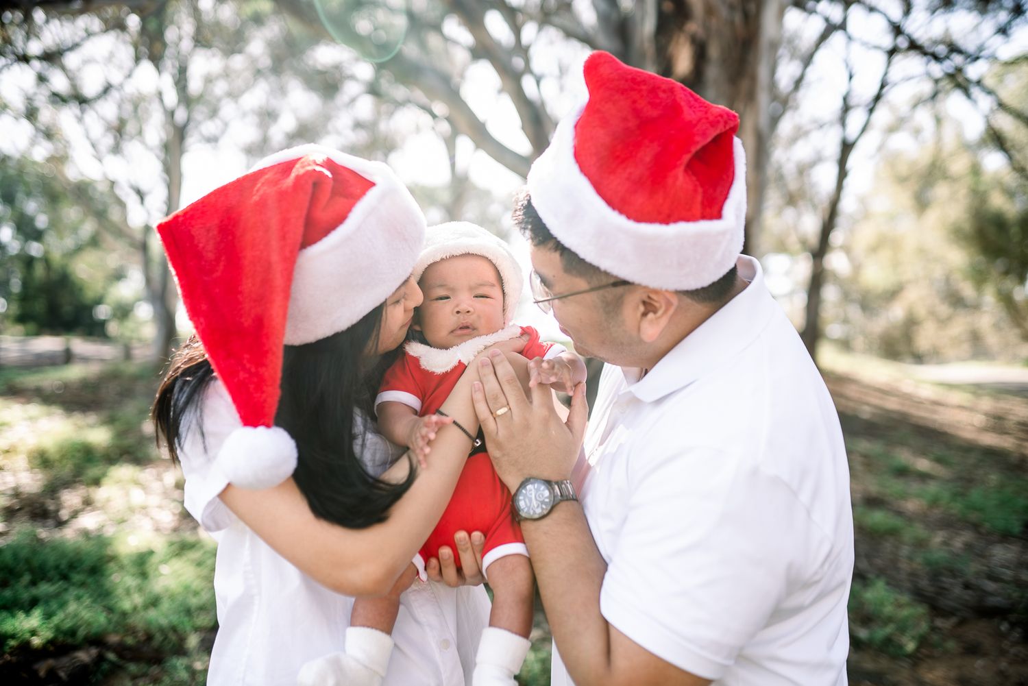 A young family in Santa hats share intimate holiday moments in a series of outdoor Chrismas Minis photo in Melbourne