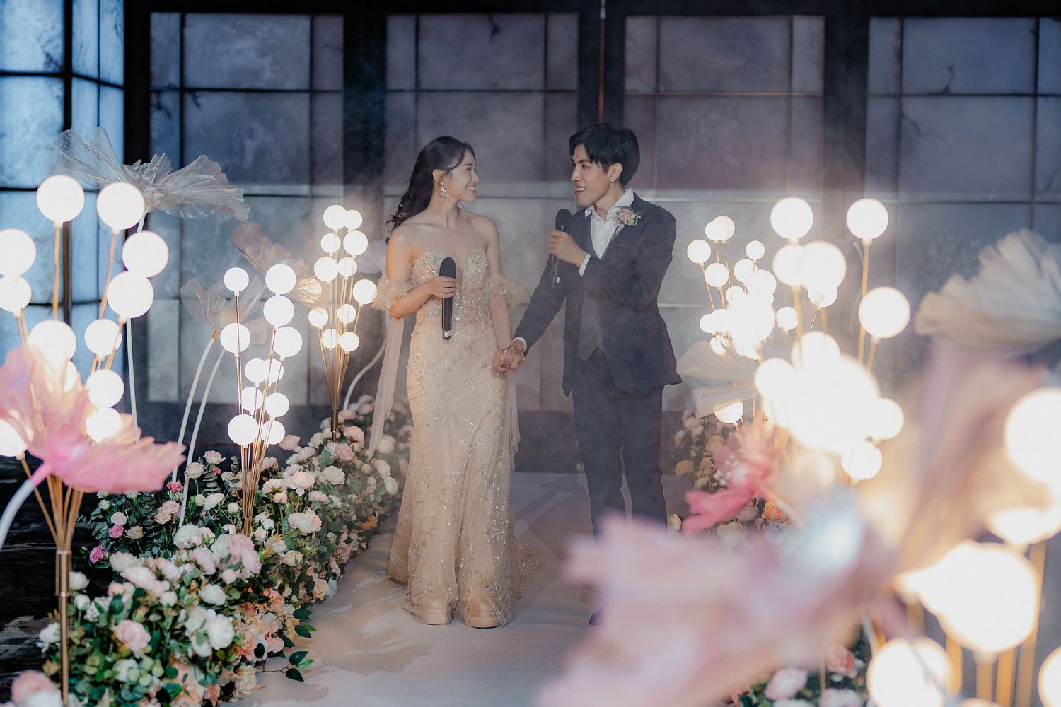 People dancing at an indoor wedding reception with white globe lights hanging from ceiling and floral decorations.