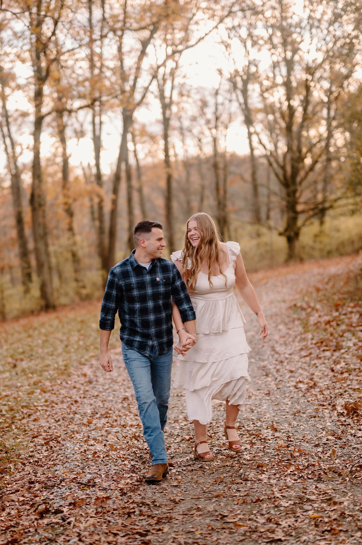 A couple holding hands while walking along a leaf-covered forest path during autumn season.