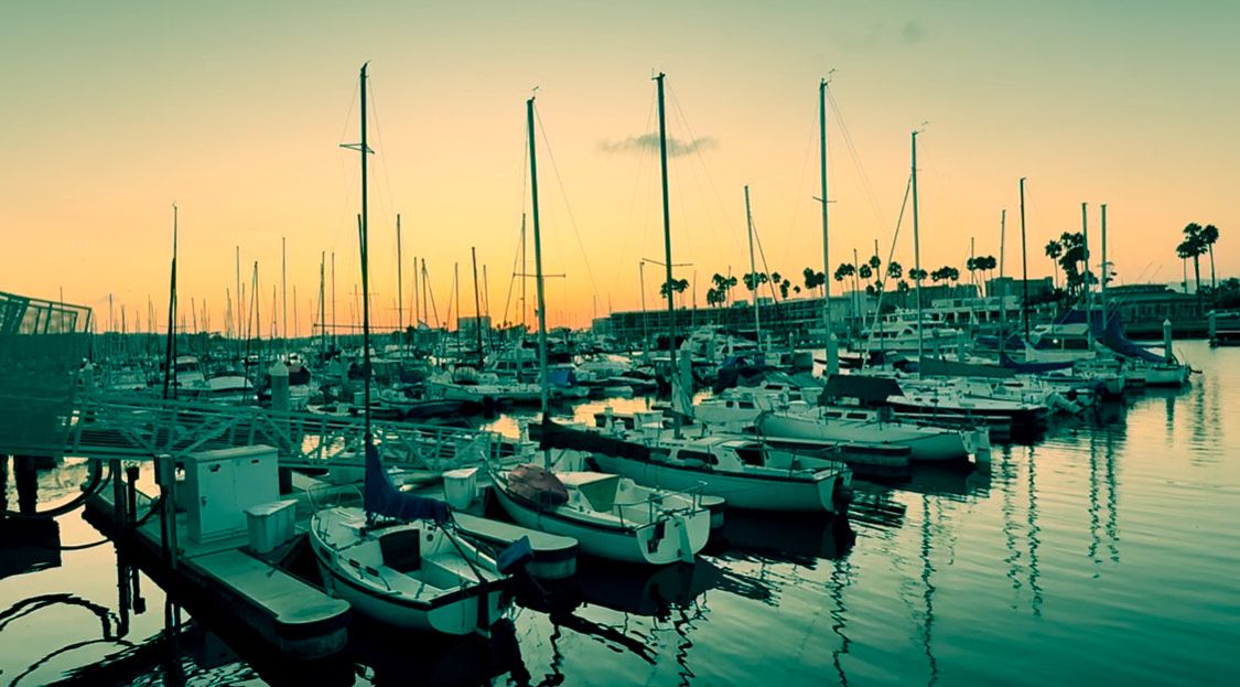 Sunset panorama of sailboats anchored in a peaceful marina with calm waters reflecting golden sky.