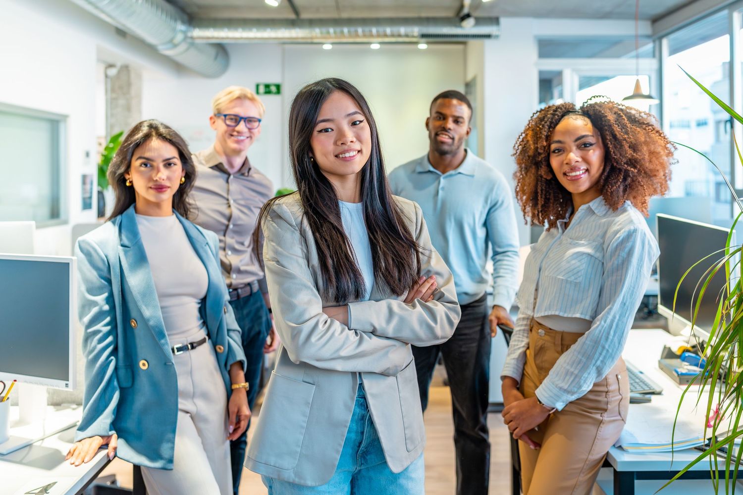 Business professionals in formal attire sit together for a group photo in a bright office setting.