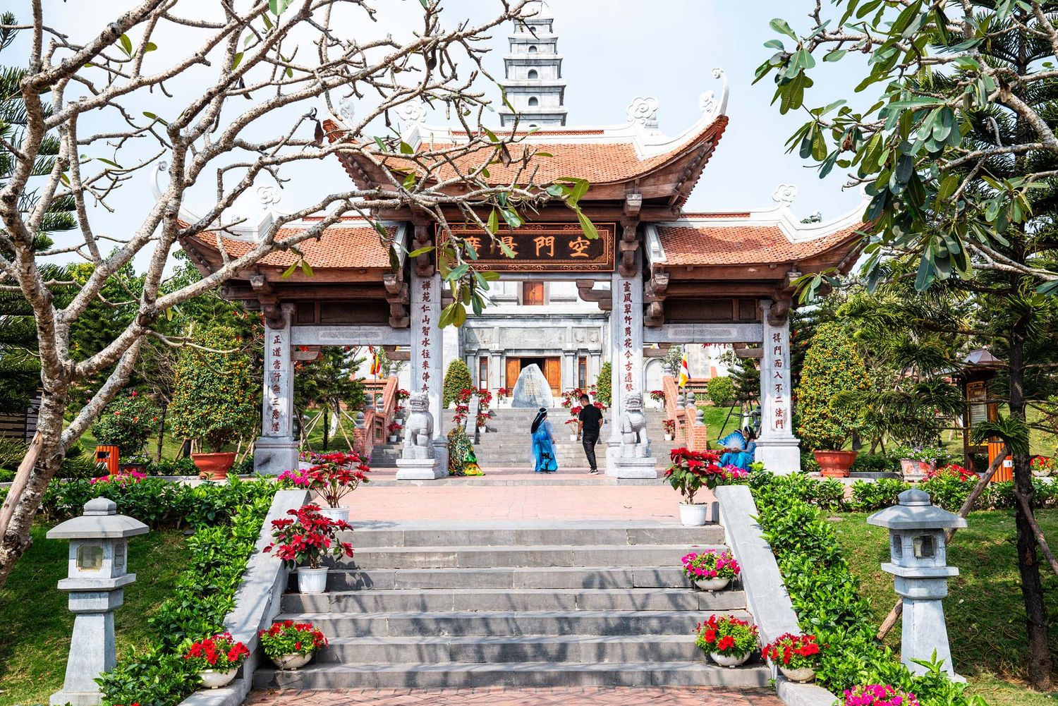 Stone steps lead to a traditional pagoda-style temple with red roofs and stone lanterns in a peaceful garden setting.