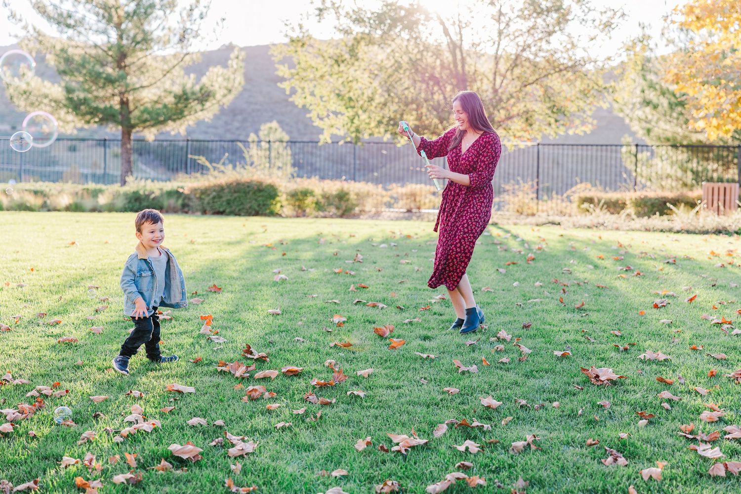 Children play and toss autumn leaves on a grassy hillside during a bright fall day.