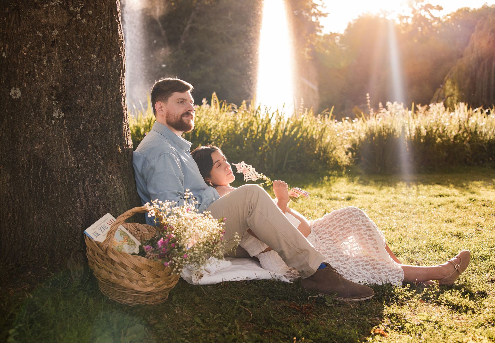 A couple enjoys a romantic sunset picnic under a tree in with sunlight streaming through the branches in Vondelpark, Amsterdam.