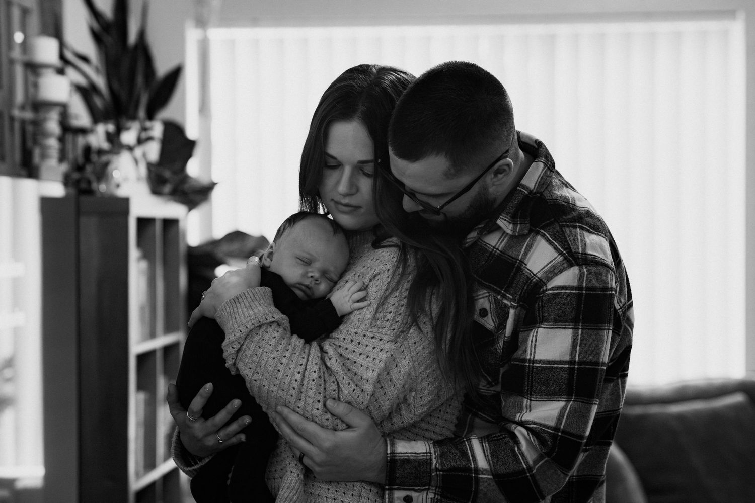 A series of black and white photos showing tender moments between parents and their baby in a home setting.