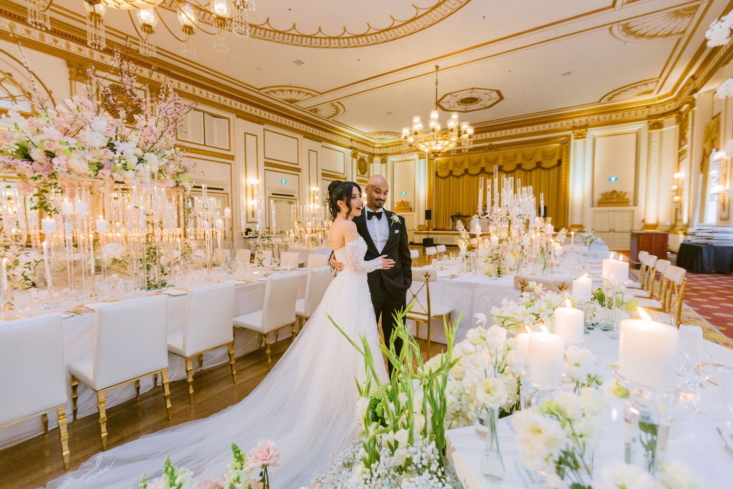 Elegant white and gold ballroom decorated with crystal chandeliers and floral centerpieces for a luxurious wedding reception.