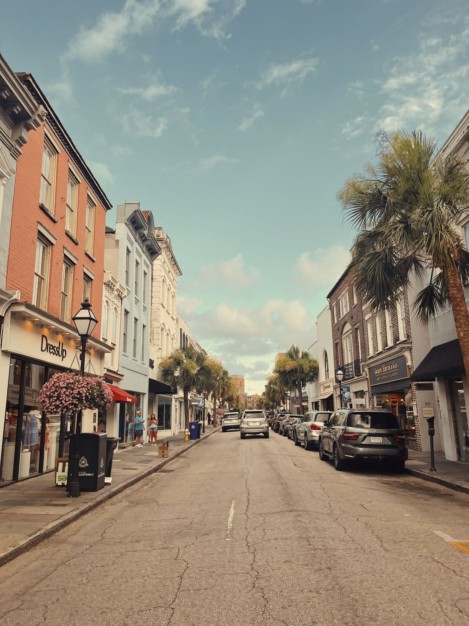 Historic downtown Charleston street with brick buildings, palm trees and parked cars on a sunny day.