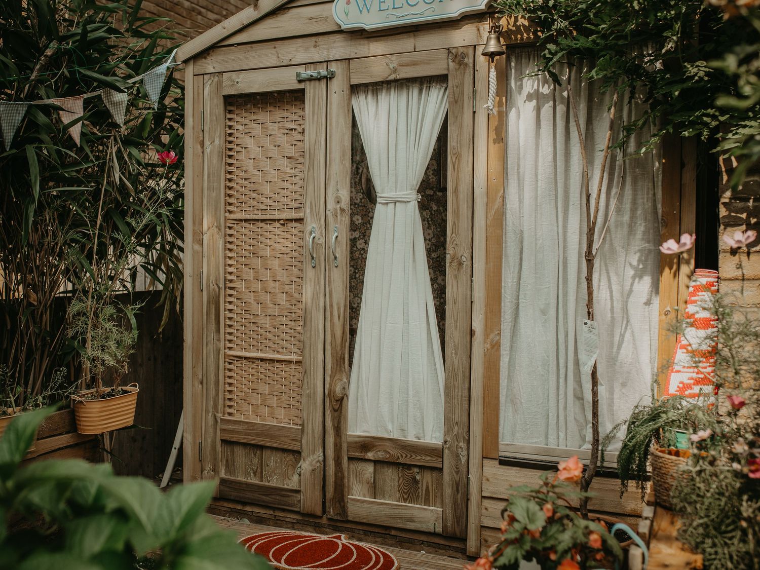 A rustic wooden door with ornate carved details leads to an outdoor garden space with soft window curtains and greenery.
