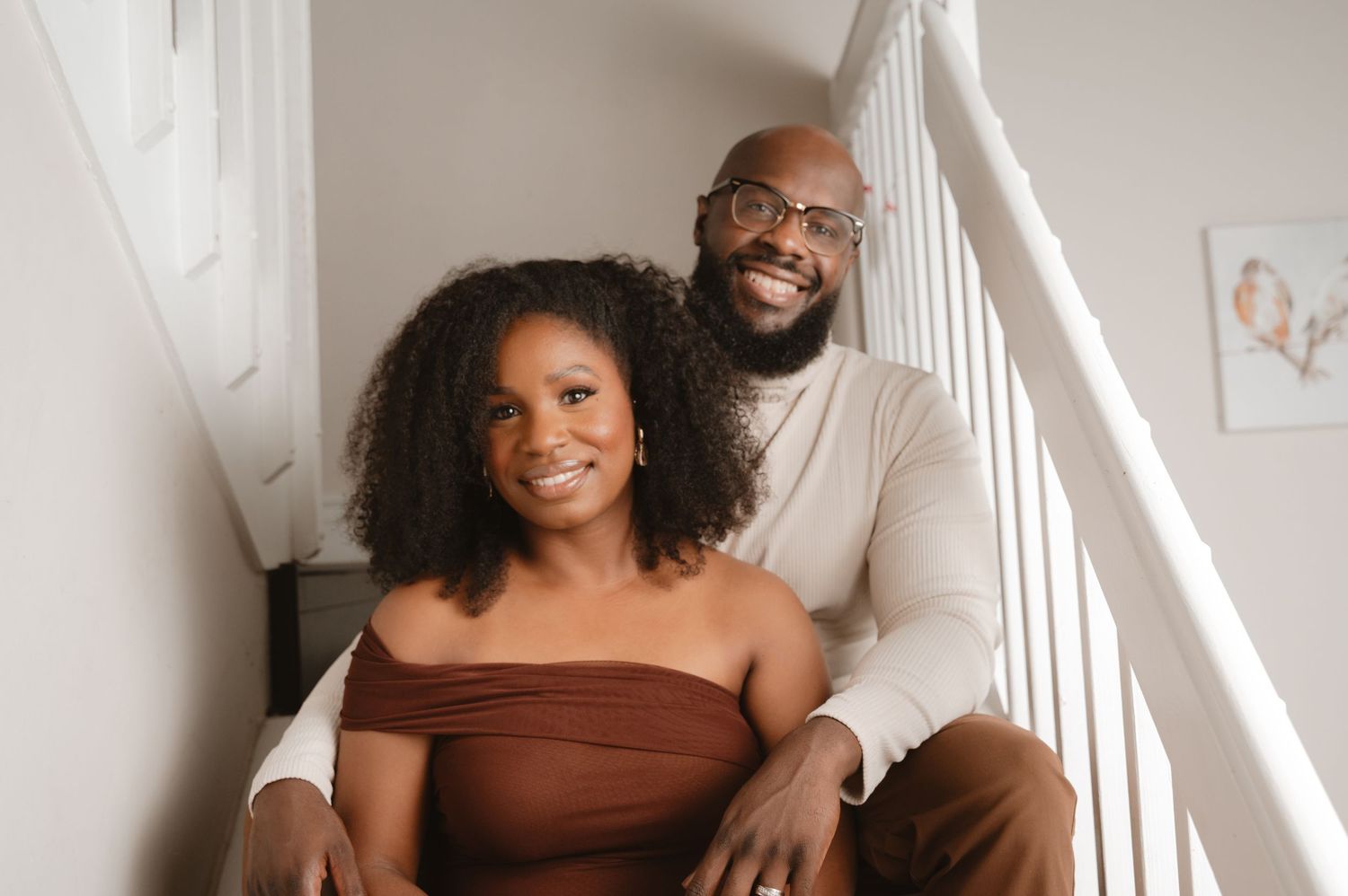 Two people sit together on white stairs in a bright interior space, sharing a warm moment.