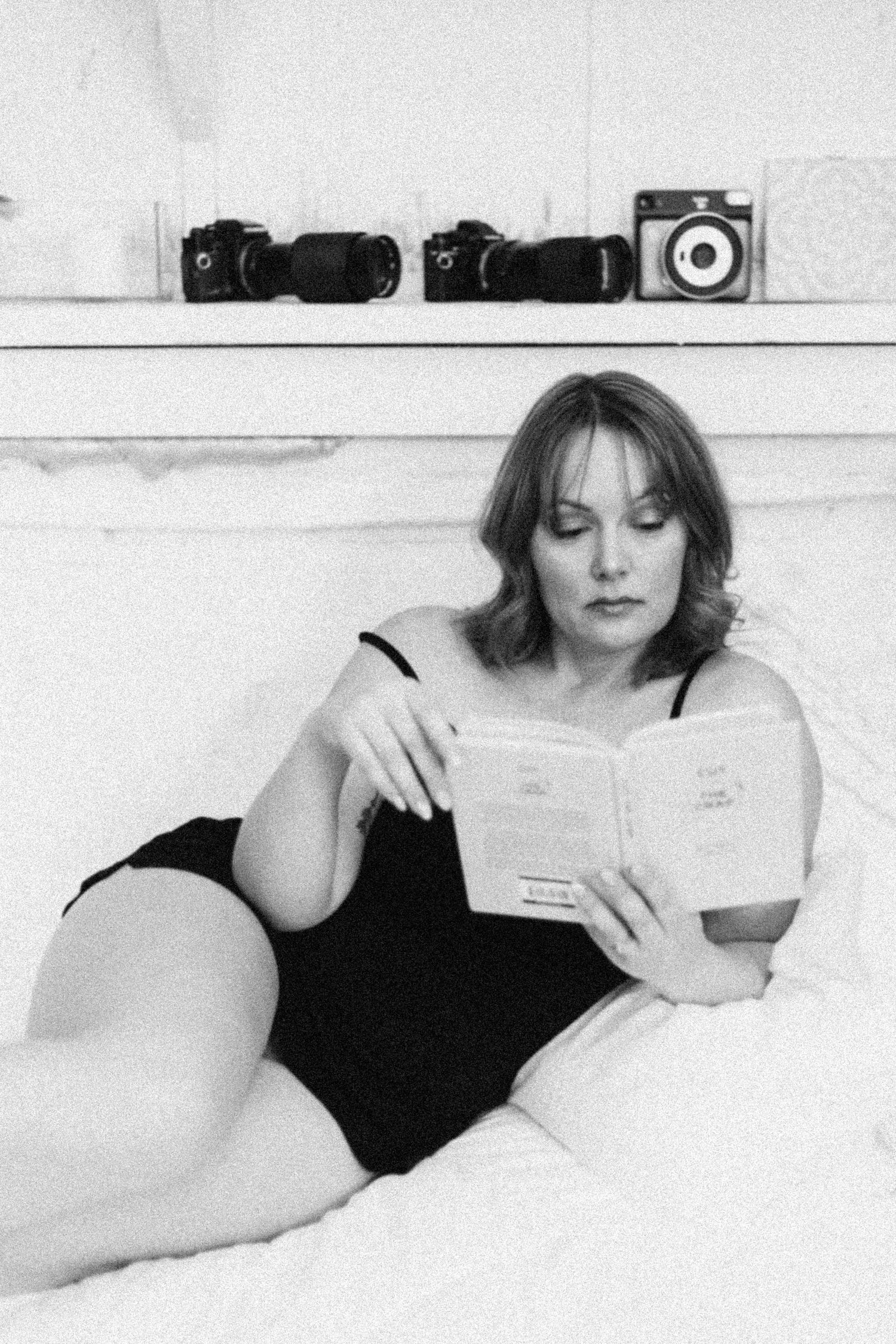 A black and white art photo series showing a figure in a black dress reclining and reading on a white surface.