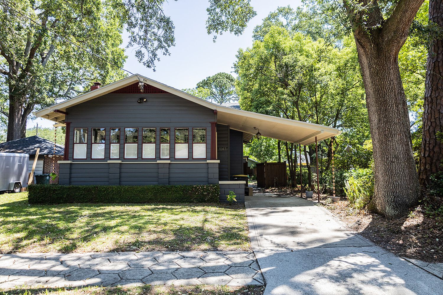 A charming craftsman bungalow house with a covered front porch and large trees providing natural shade.