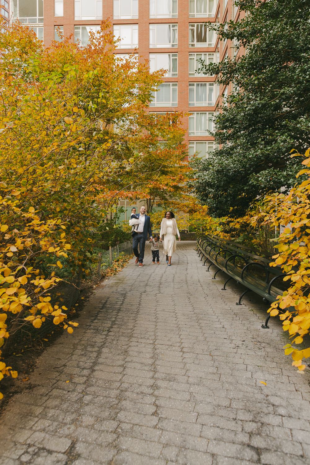Family of four walking through autumn leaves in a Tribeca park, NYC.