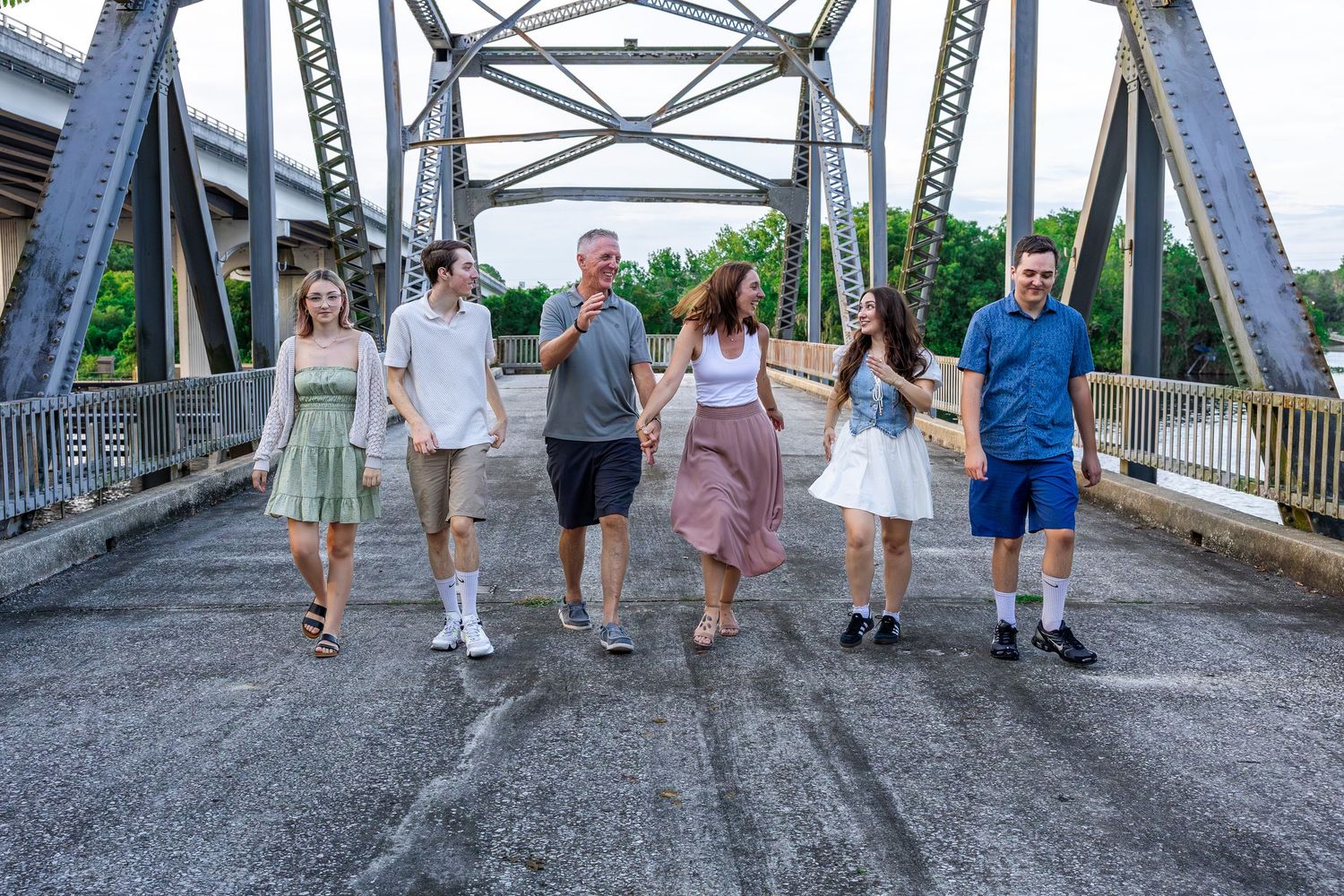 People walking together on a metal bridge in casual summer clothing.
