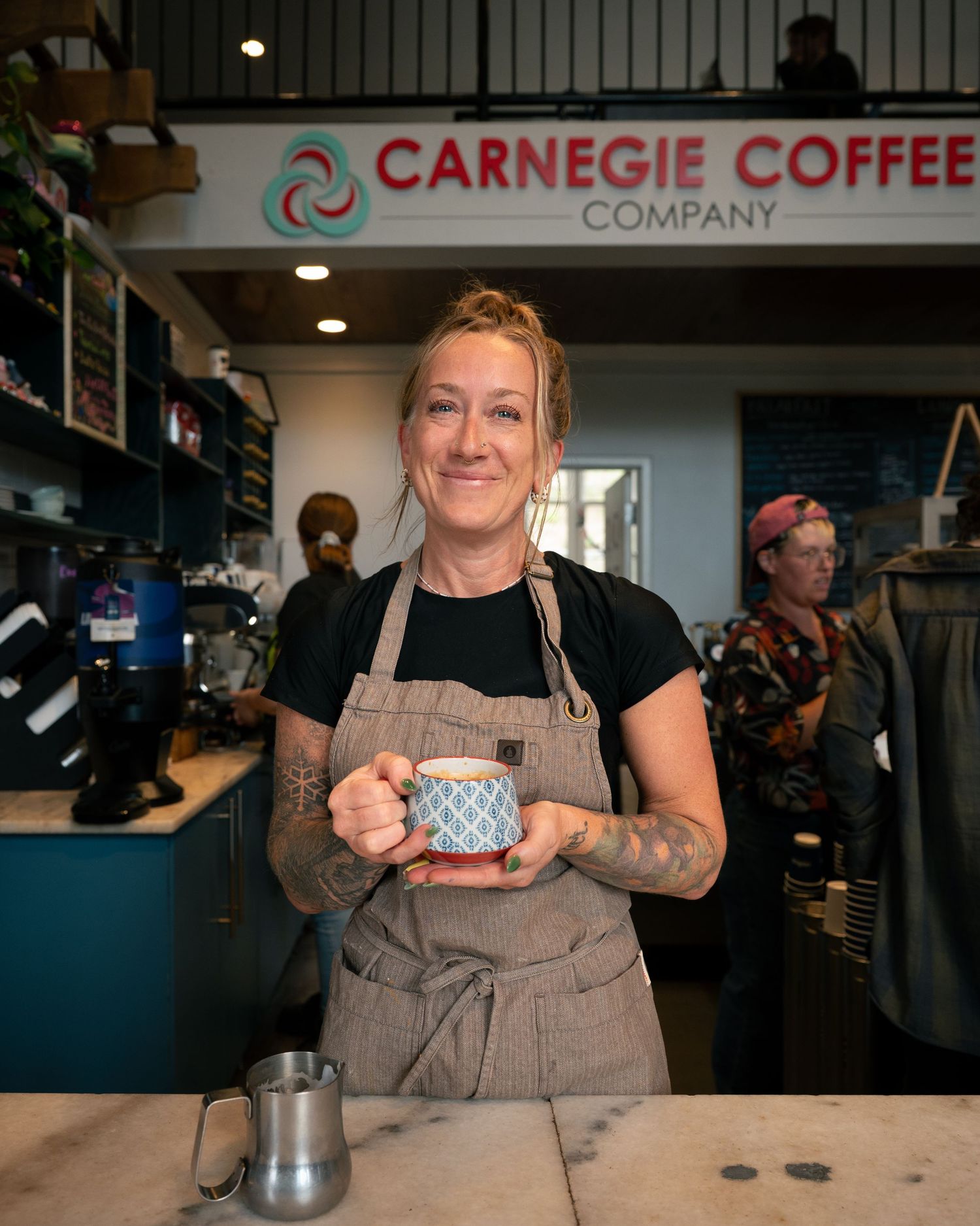 A barista wearing a brown apron serves coffee at Carnegie Coffee Company's counter.