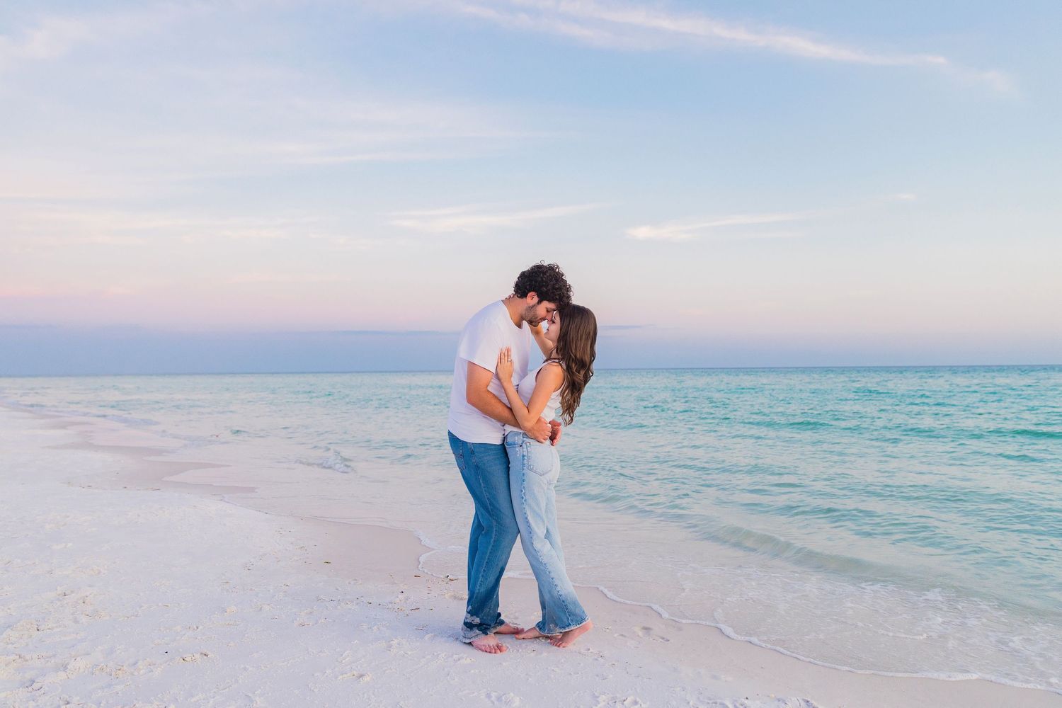 A romantic beach proposal at sunset with turquoise waters and sandy shoreline in the background.
