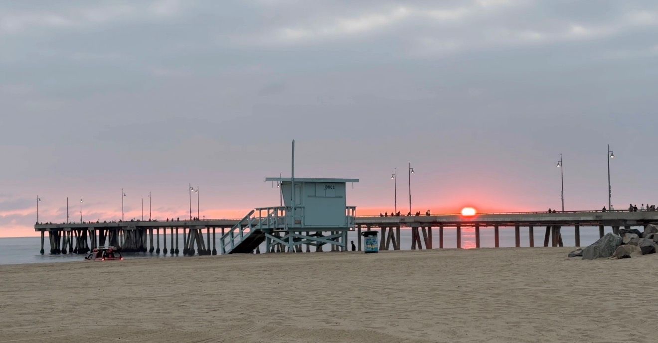 Scenic panoramic view of a wooden pier stretching into the ocean at sunset with orange sky reflecting on calm waters.