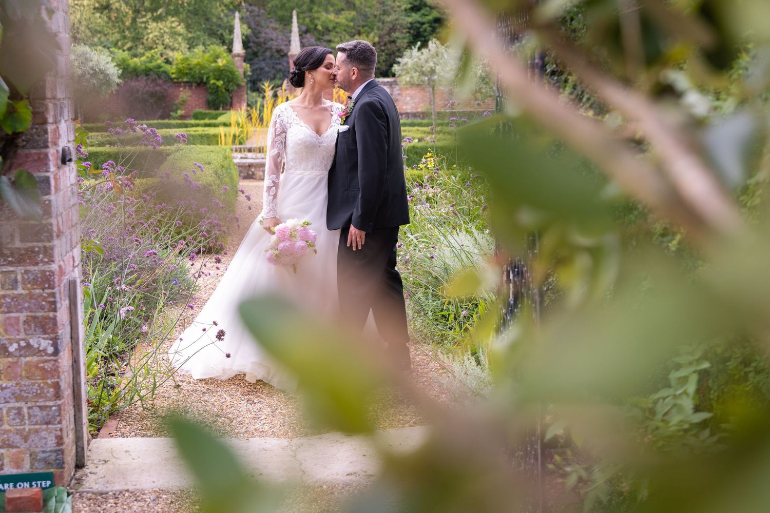 Bride and groom share a romantic kiss in a lush garden setting on their wedding day.