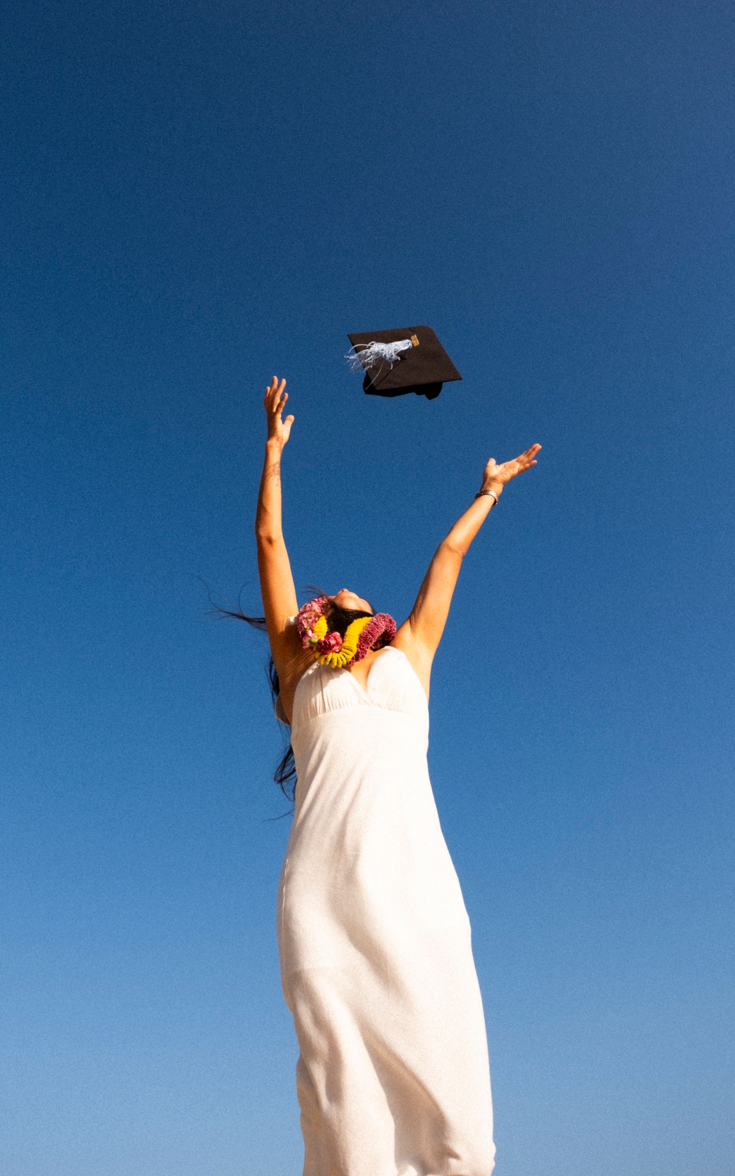 Graduate celebrating with cap toss during a Hawaii graduation photography session beneath a clear blue sky.