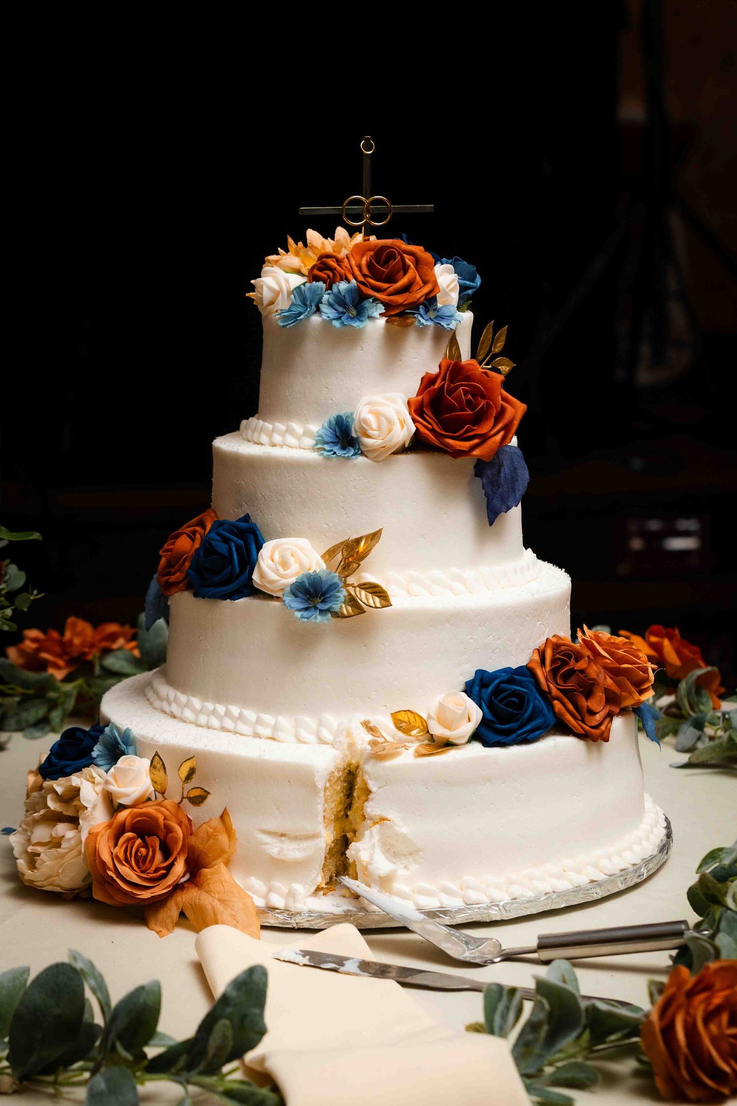 An ornate tiered wedding cake, decorated with edible flowers, gold leaves, and frosting patterns.