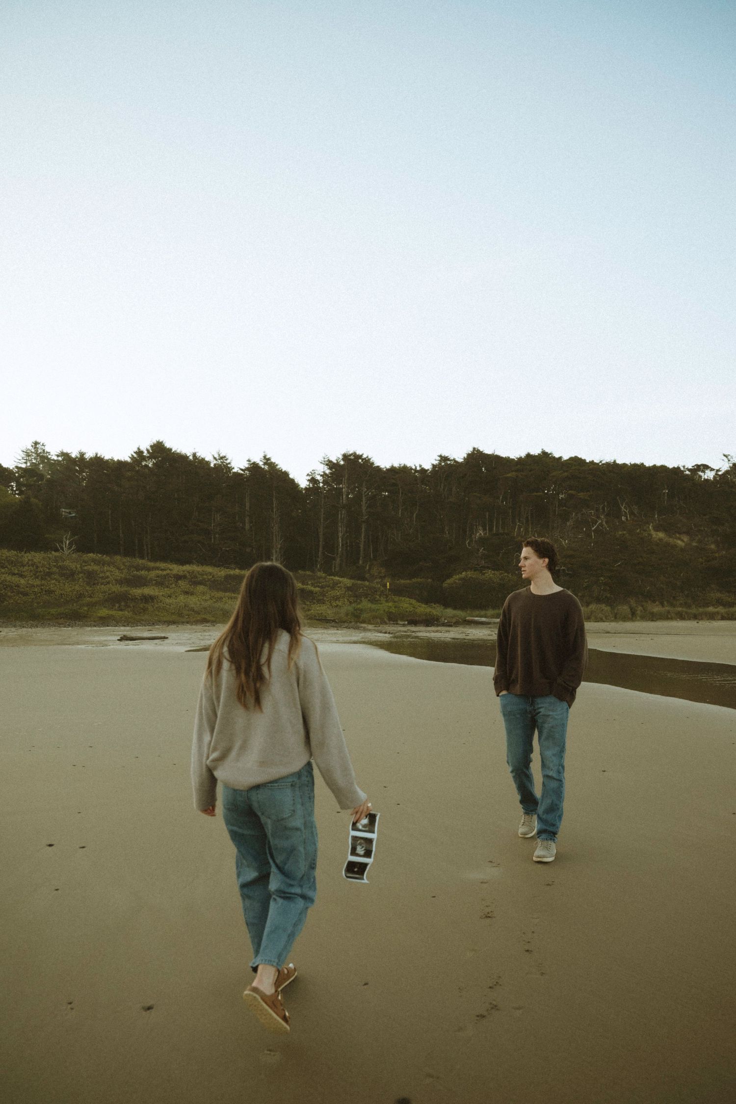 couple stand silhouetted against dramatic rocky cliffs during golden hour creating a moody coastal landscape scene.