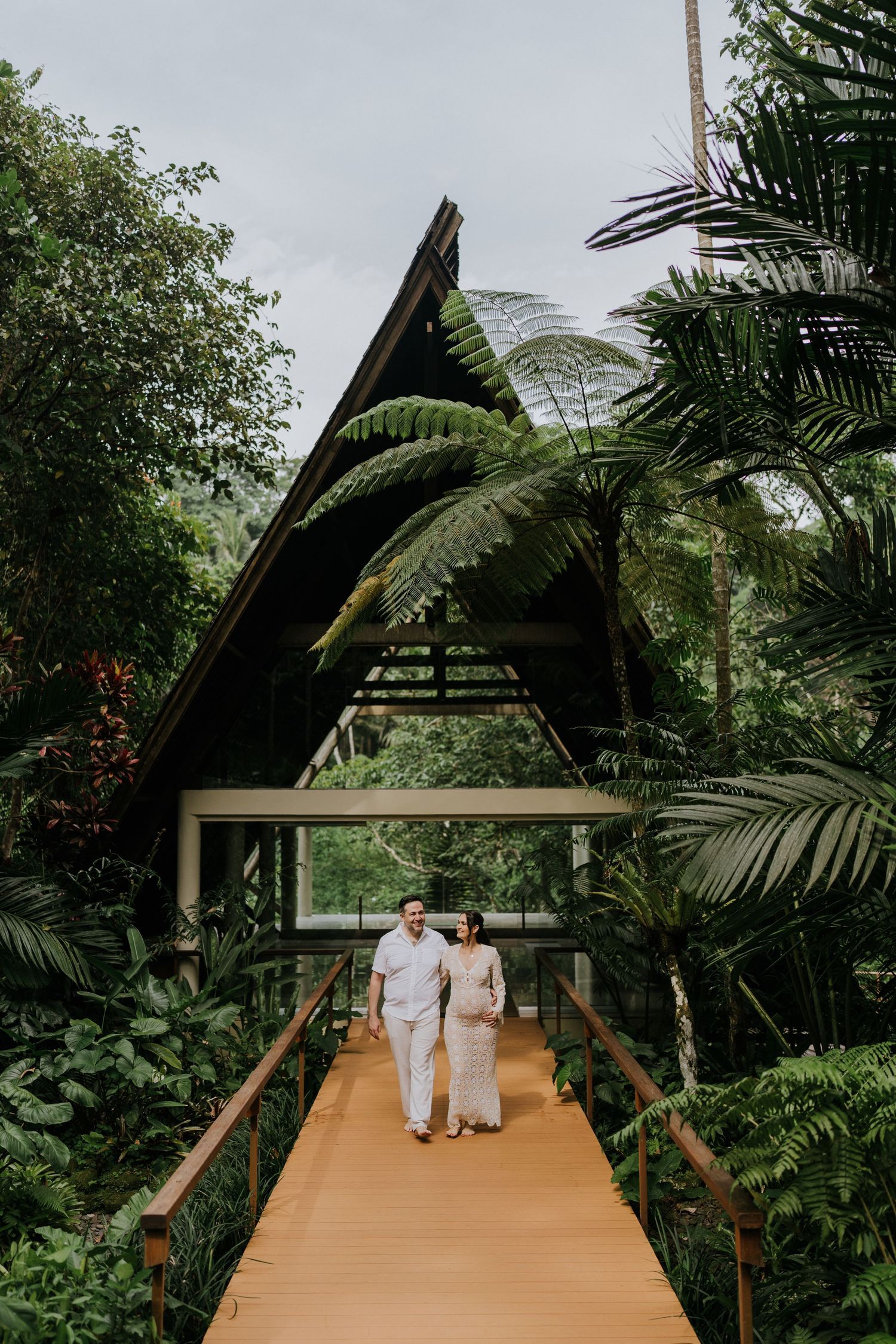 Couple walking along a green garden pathway surrounded by tropical plants.