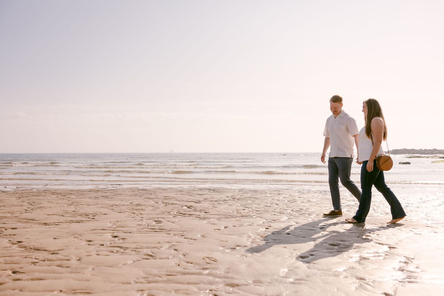 A couple stroll along a sunny North East beach in Tynemouth during their engagement shoot