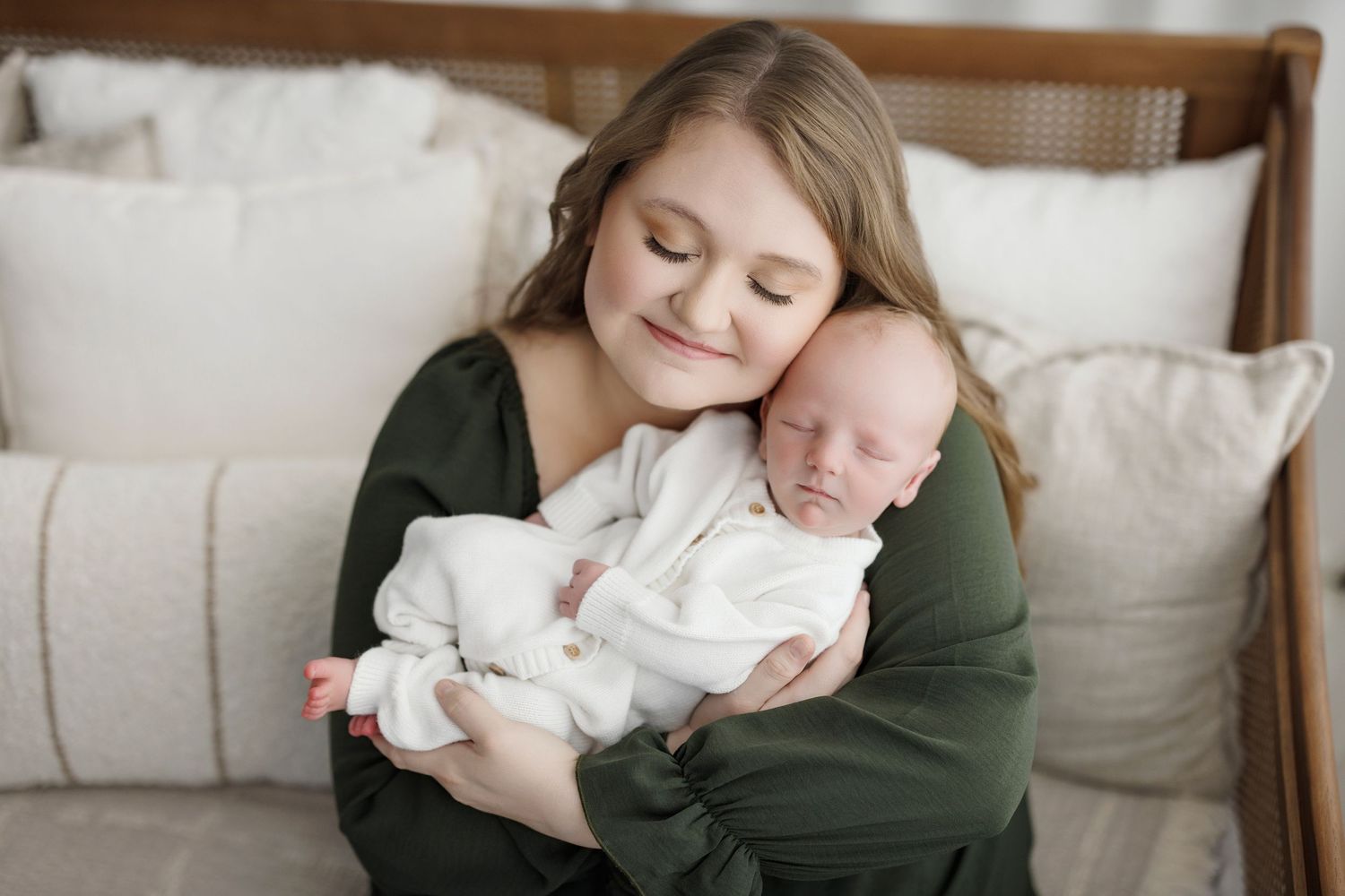 A smiling young girl in a green dress gently holds a sleeping newborn baby wrapped in white.