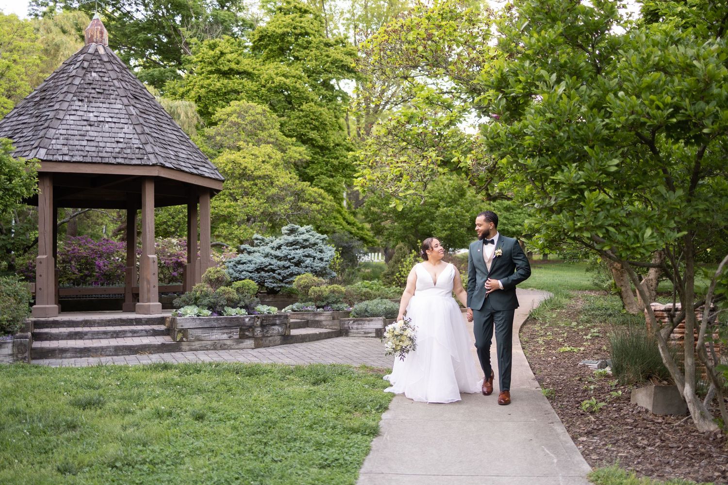Couple sharing a tender kiss on a winding park path at golden hour with a fountain in the background.