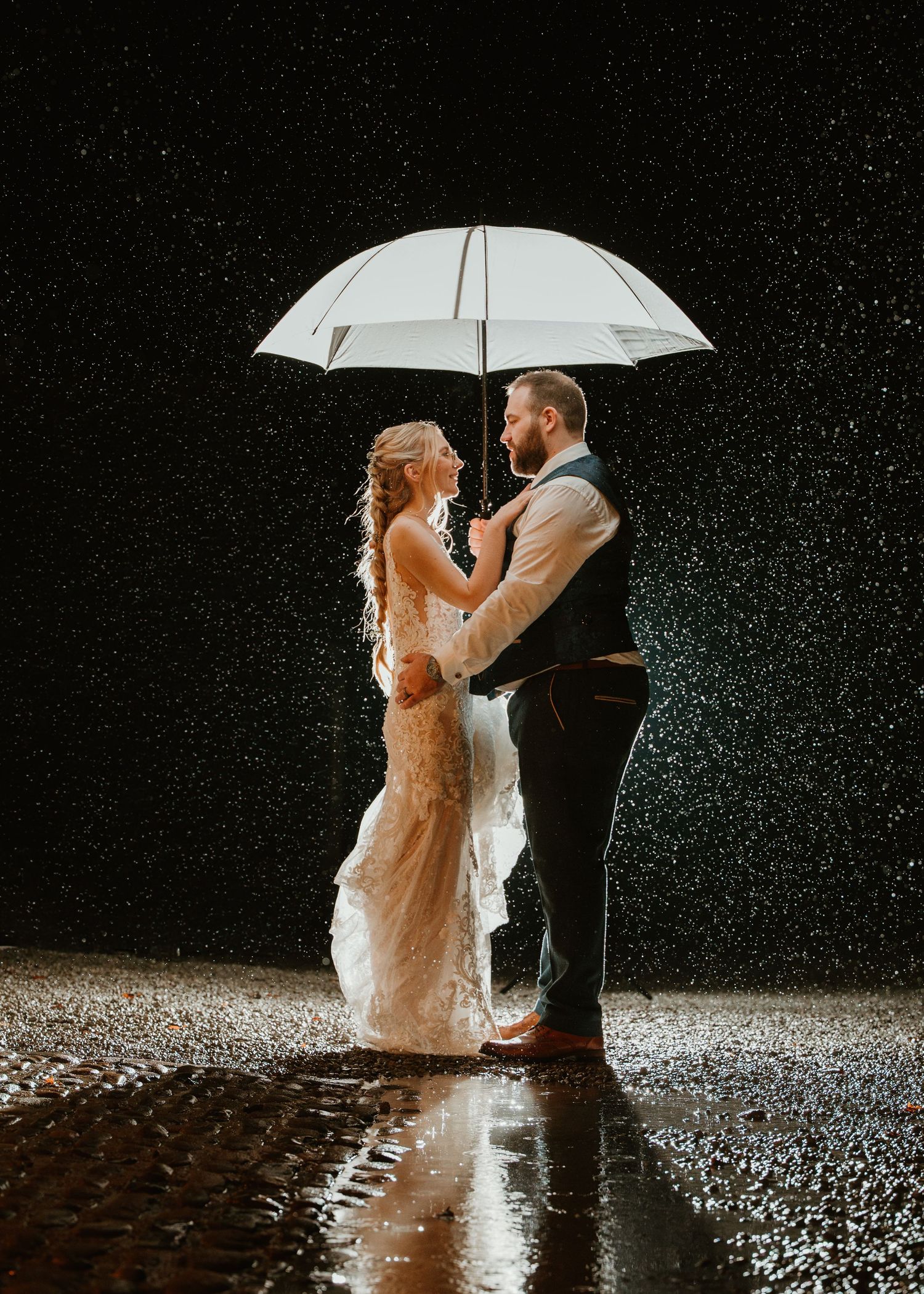 A romantic black and white photo of a couple sharing a moment under a white umbrella in the rain.