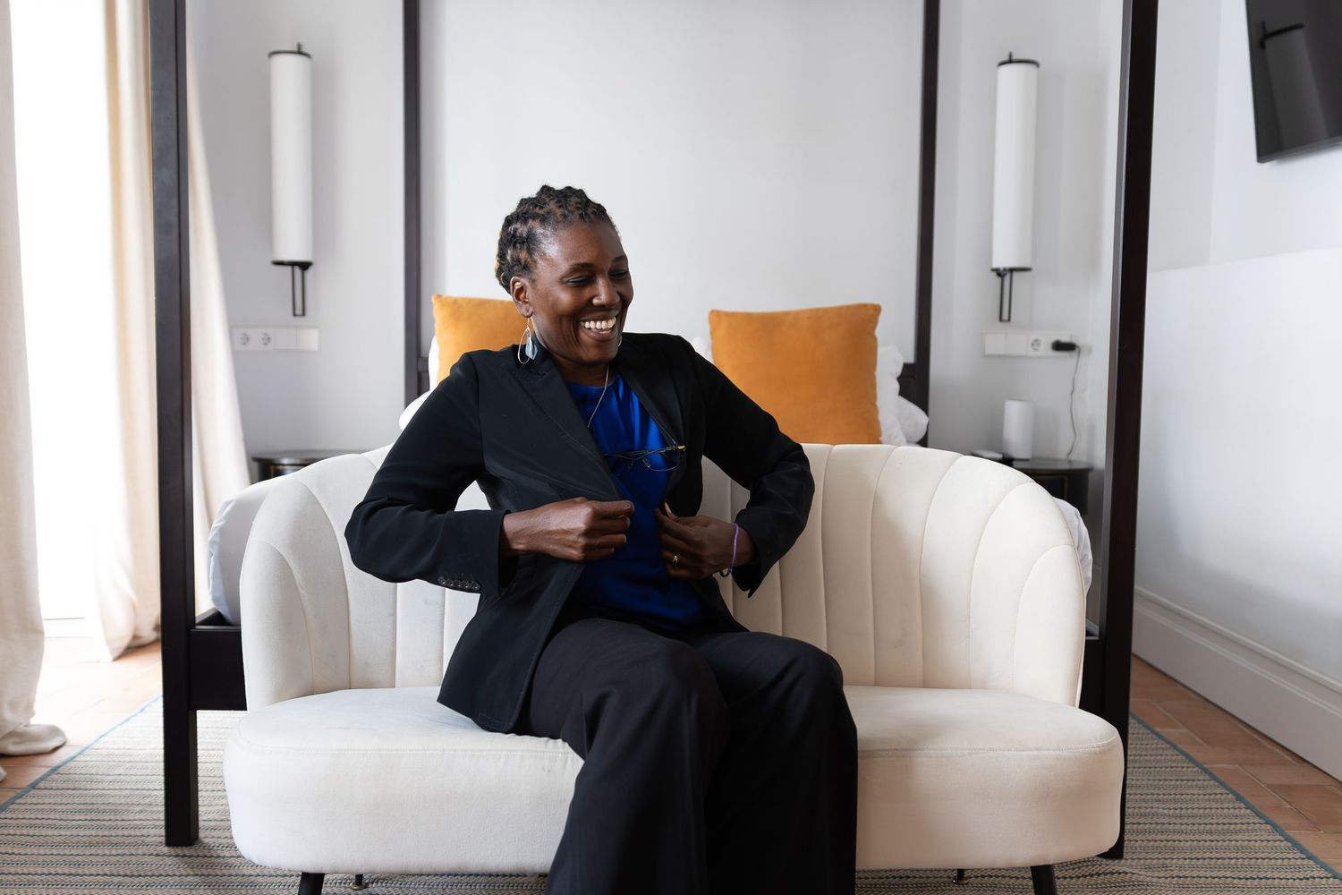 Person in a black coat sits on a white sofa in a modern interior space with wall sconces.