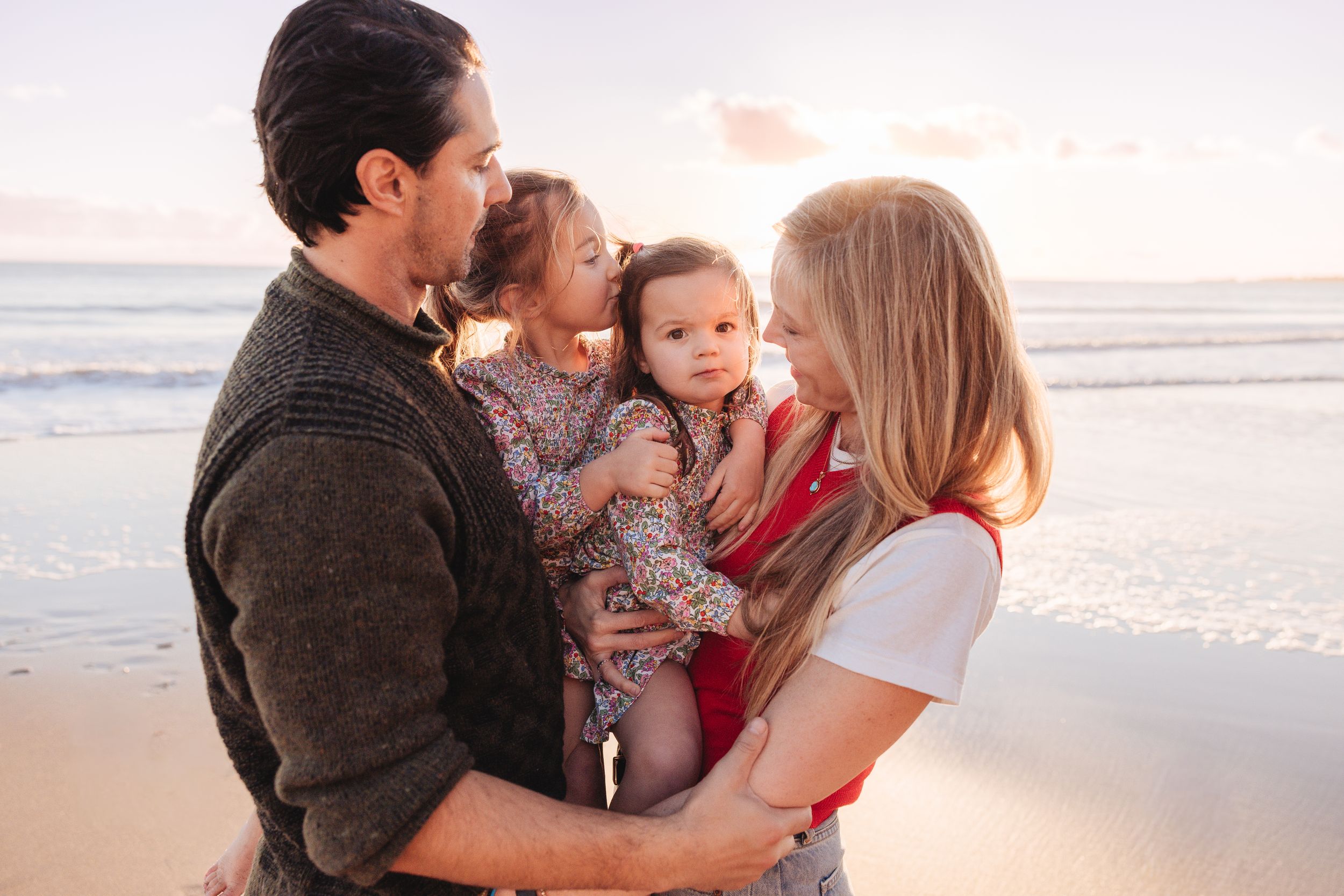 A loving family shares tender moments together on a sunny beach at sunset.