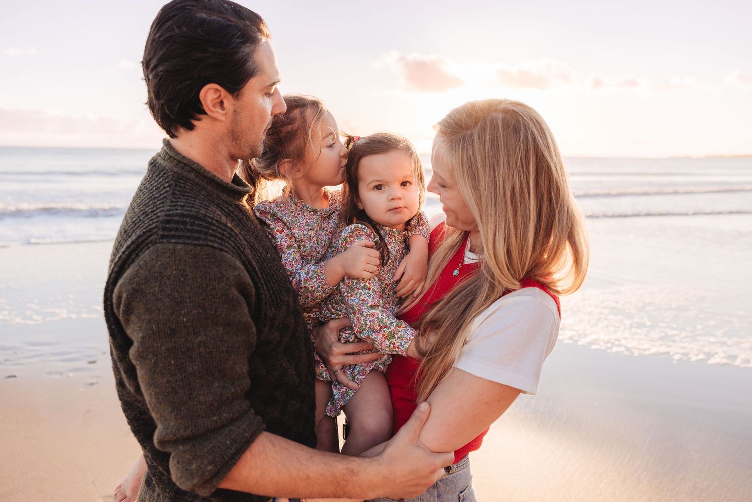 A loving family shares tender moments together on a sunny beach at sunset.