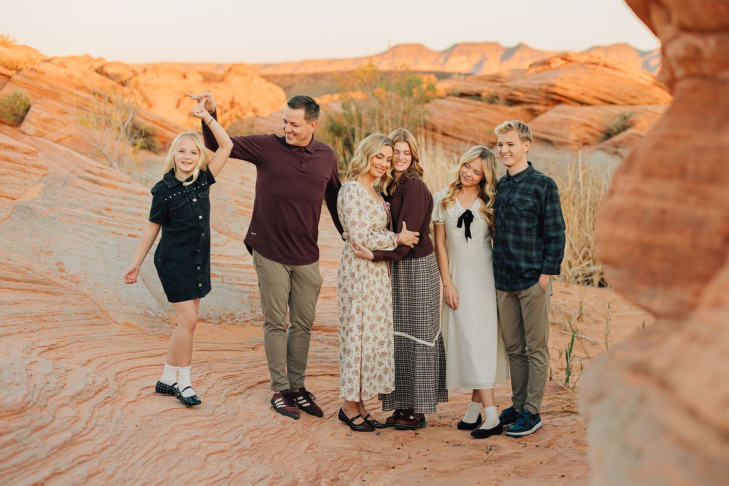 Family of six posing together among red rock formations at golden hour in a desert canyon landscape.