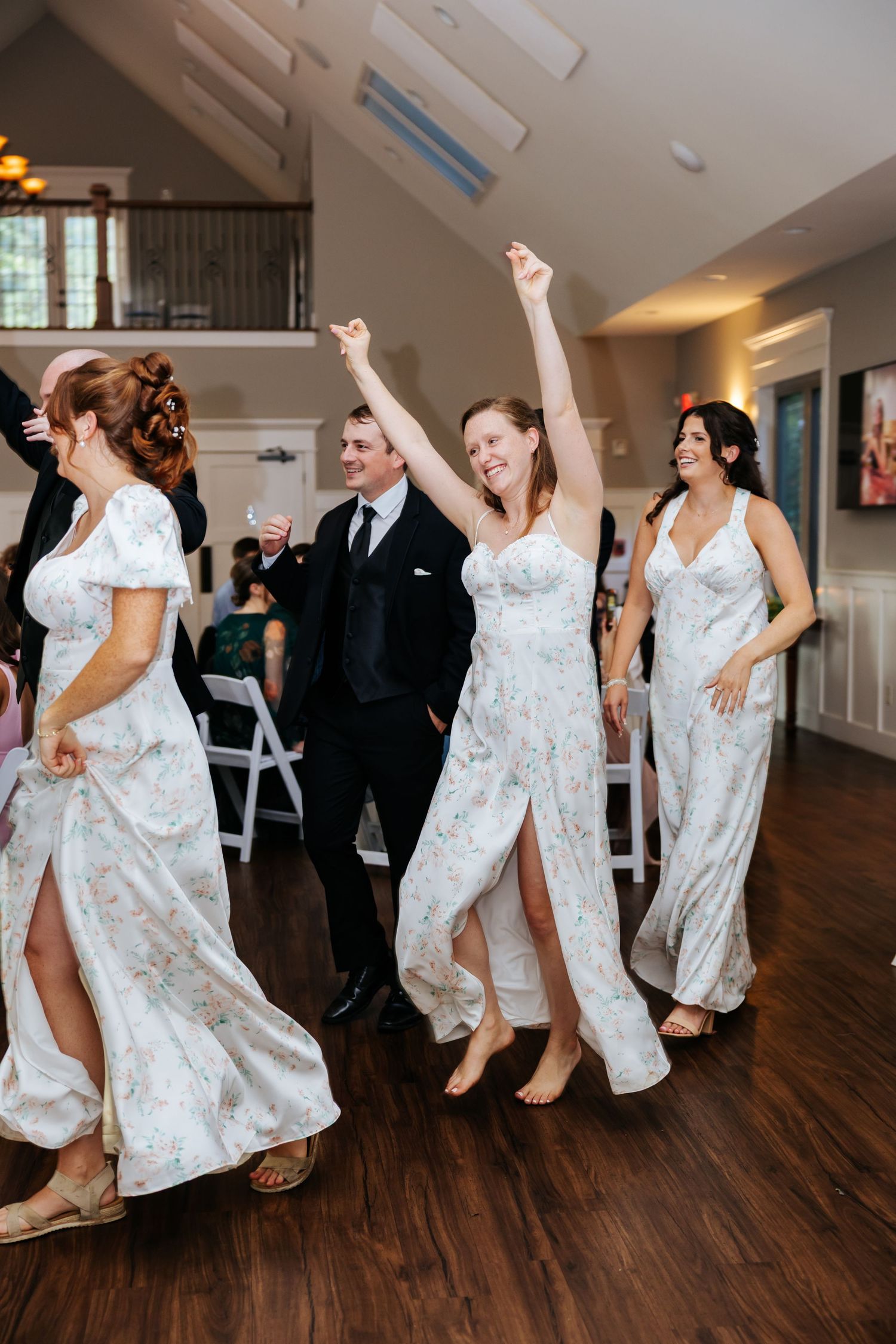 Wedding party guests dance and celebrate on a polished hardwood floor at an indoor reception venue.