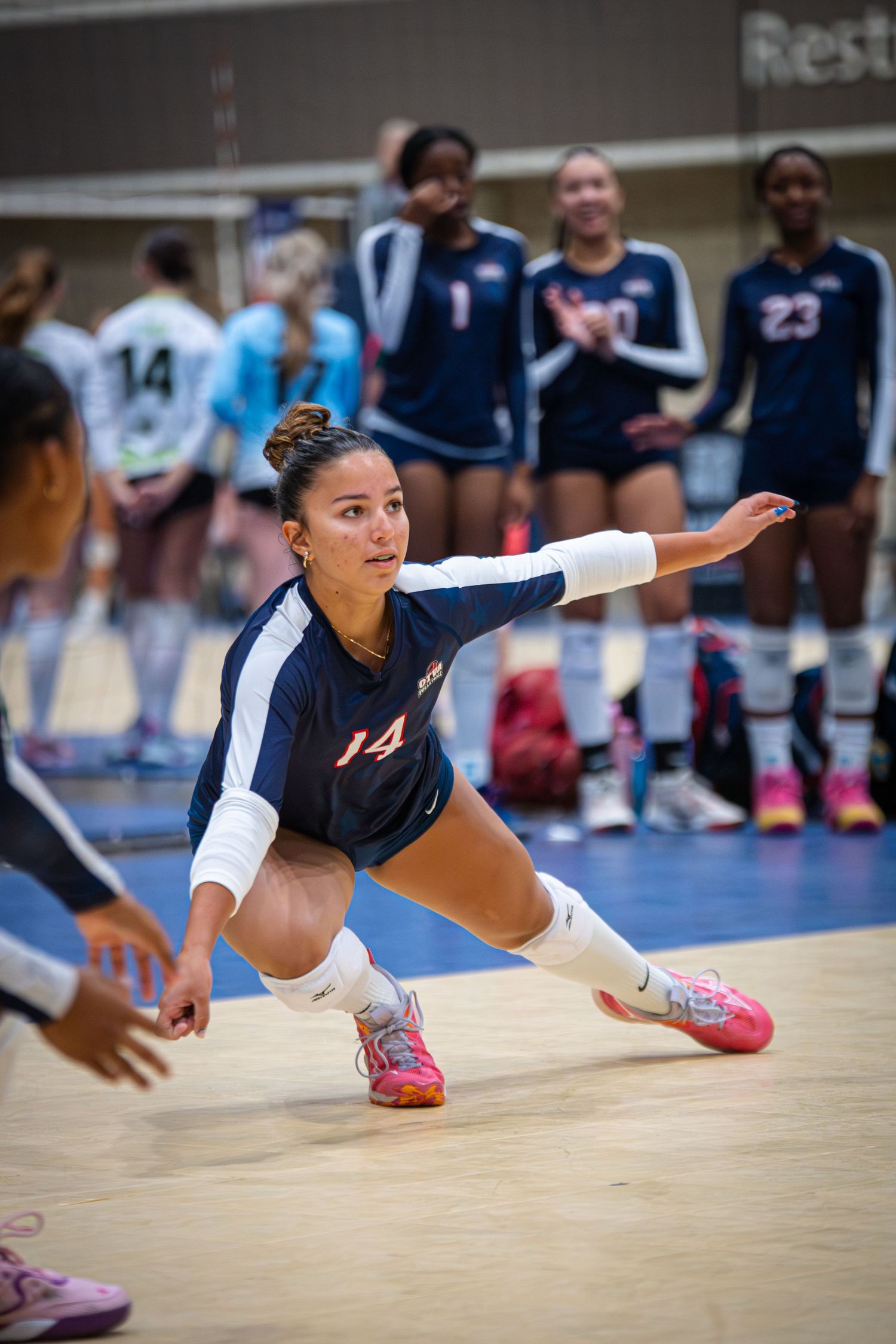 Female volleyball player #20 sets the ball during an indoor tournament match while teammate #33 prepares to spike.