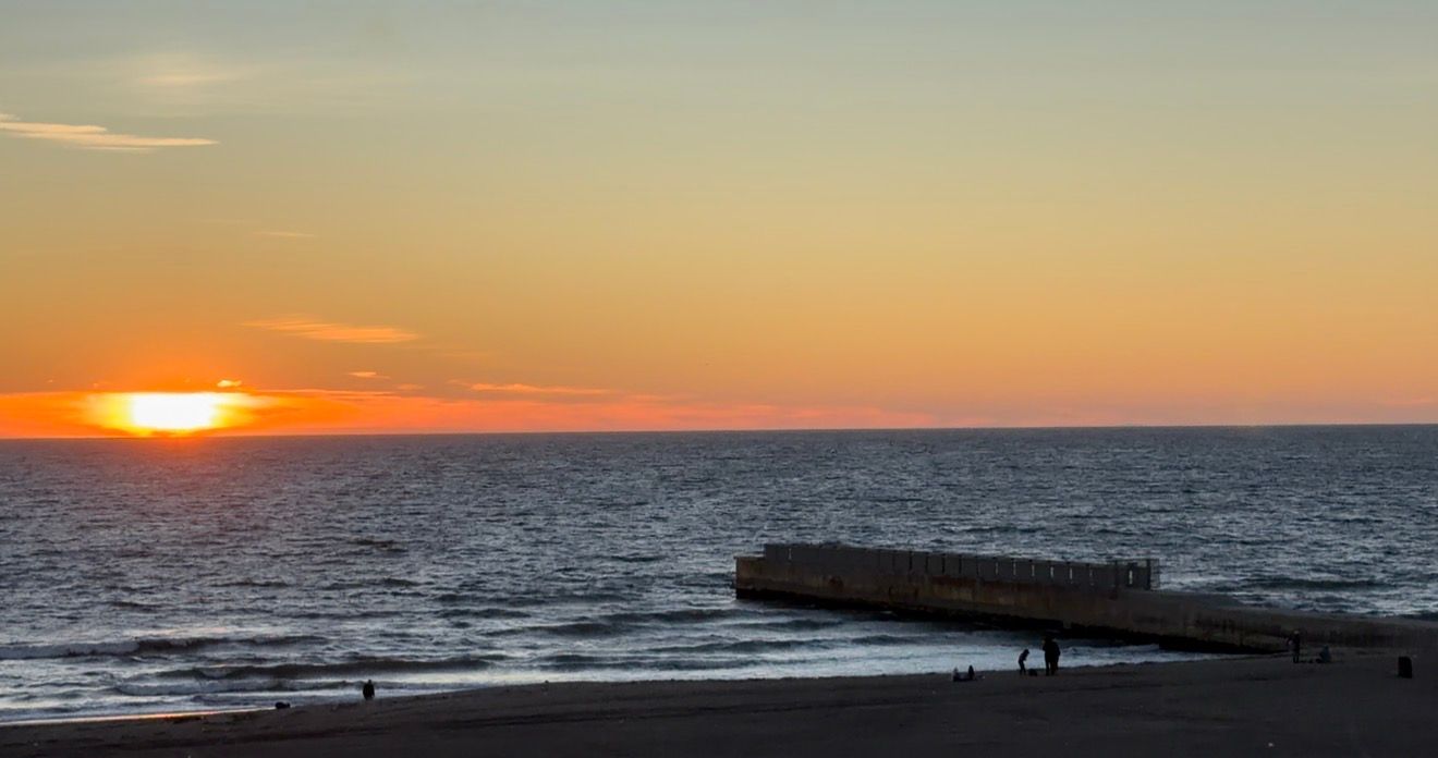 A stunning panoramic view of a sunset over the ocean with a stone pier extending into the calm waters.
