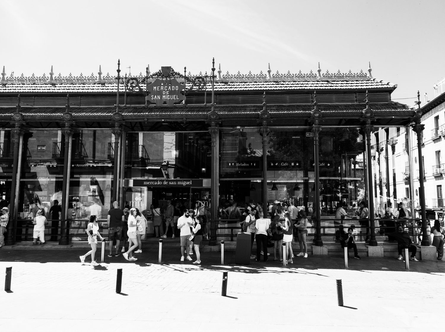 Black and white photo of Mercado de San Miguel market facade with crowds of tourists outside in Madrid Spain.