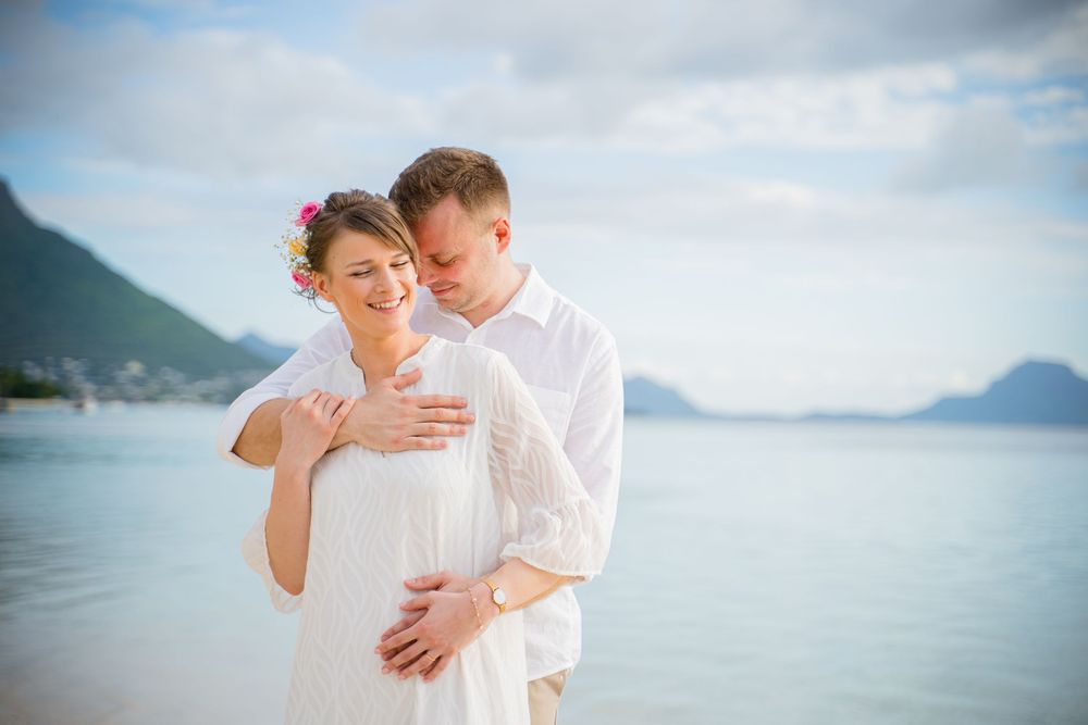 A romantic couple shares tender moments on a scenic beach with mountains and ocean in the background. Shot by Luminair Studio