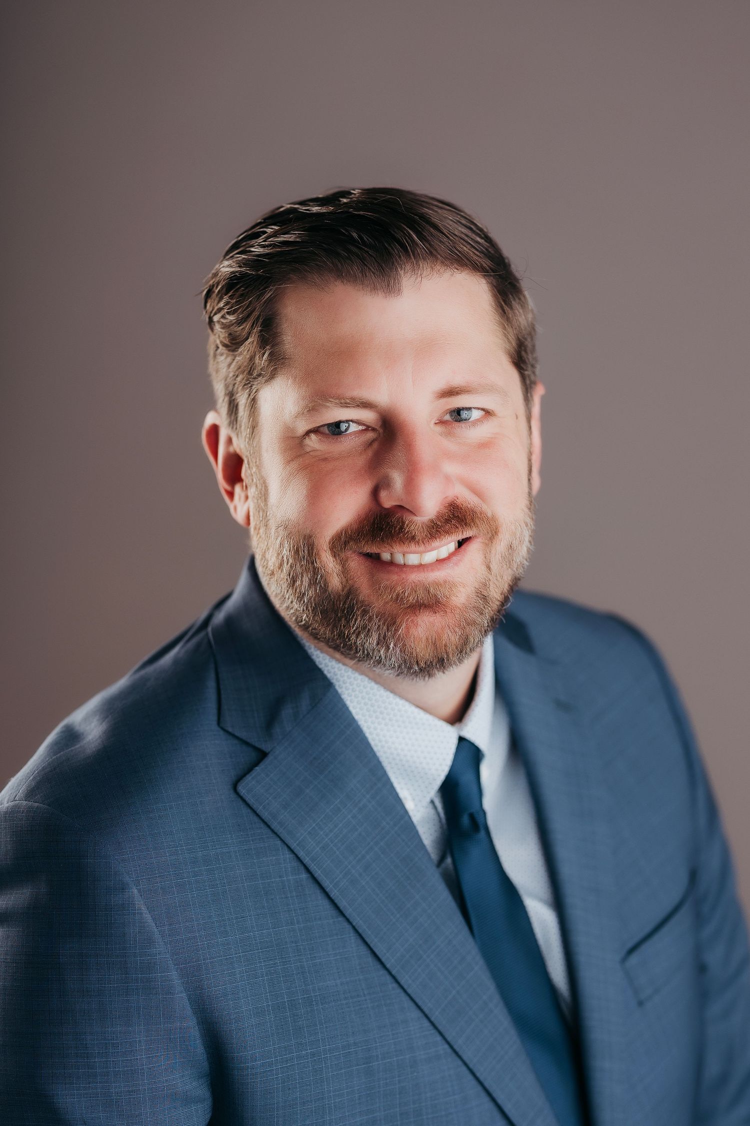 Professional headshot series of someone in a navy blue suit against a neutral gray background.