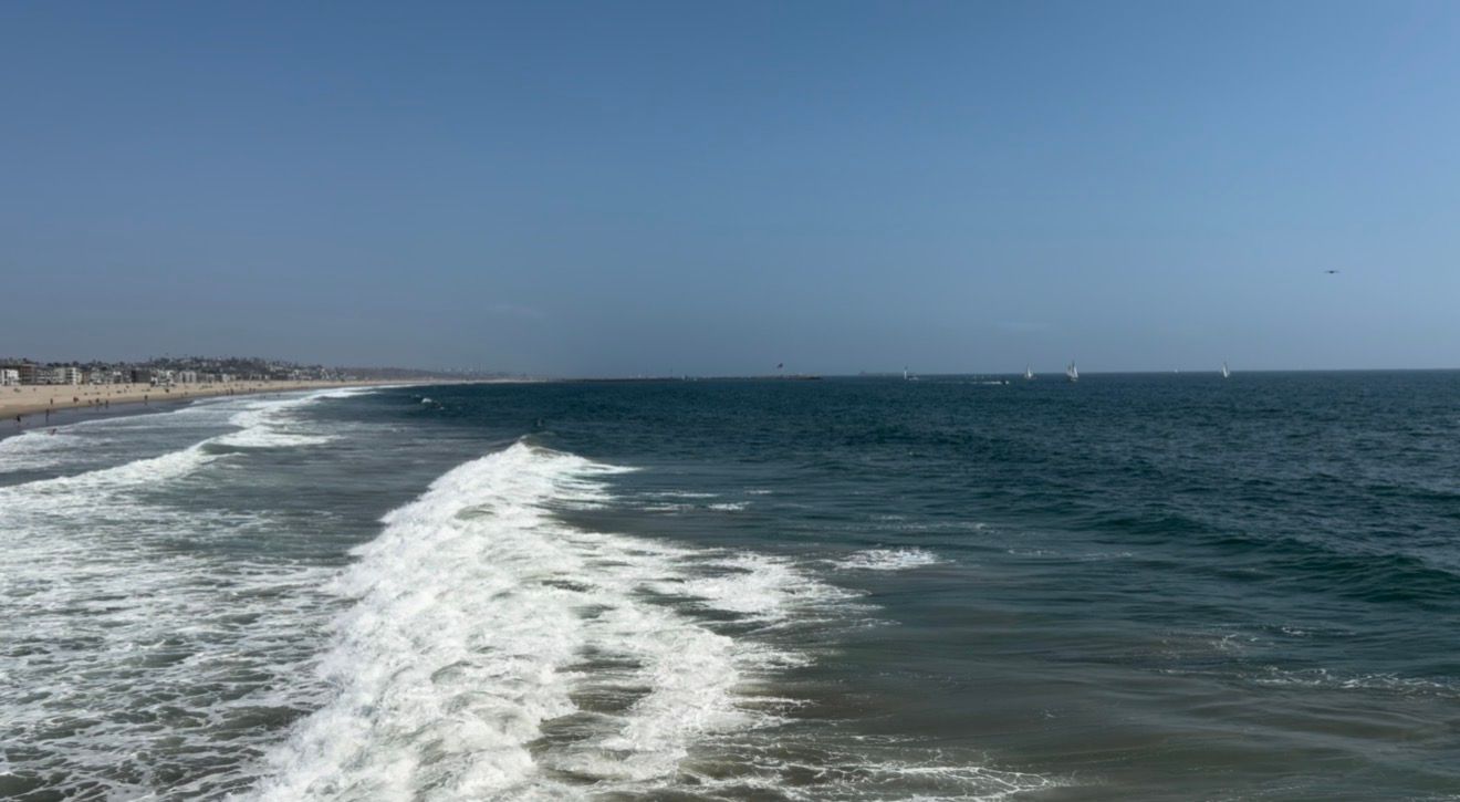 Ocean waves crash along a sandy beach coastline under a clear blue sky on a sunny day.