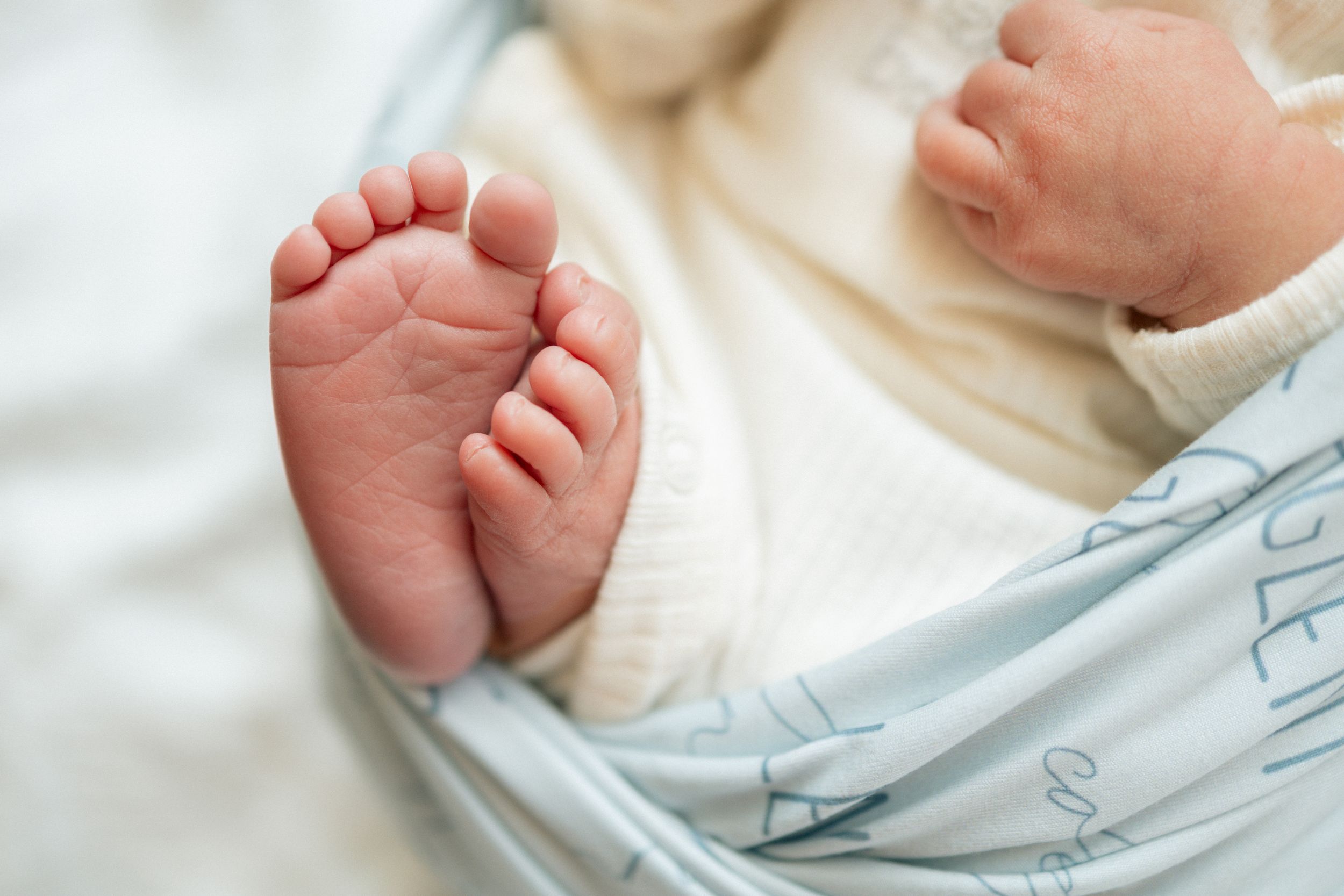 Close-up of tiny newborn baby feet wrapped in a soft white swaddle blanket in a hospital setting.
