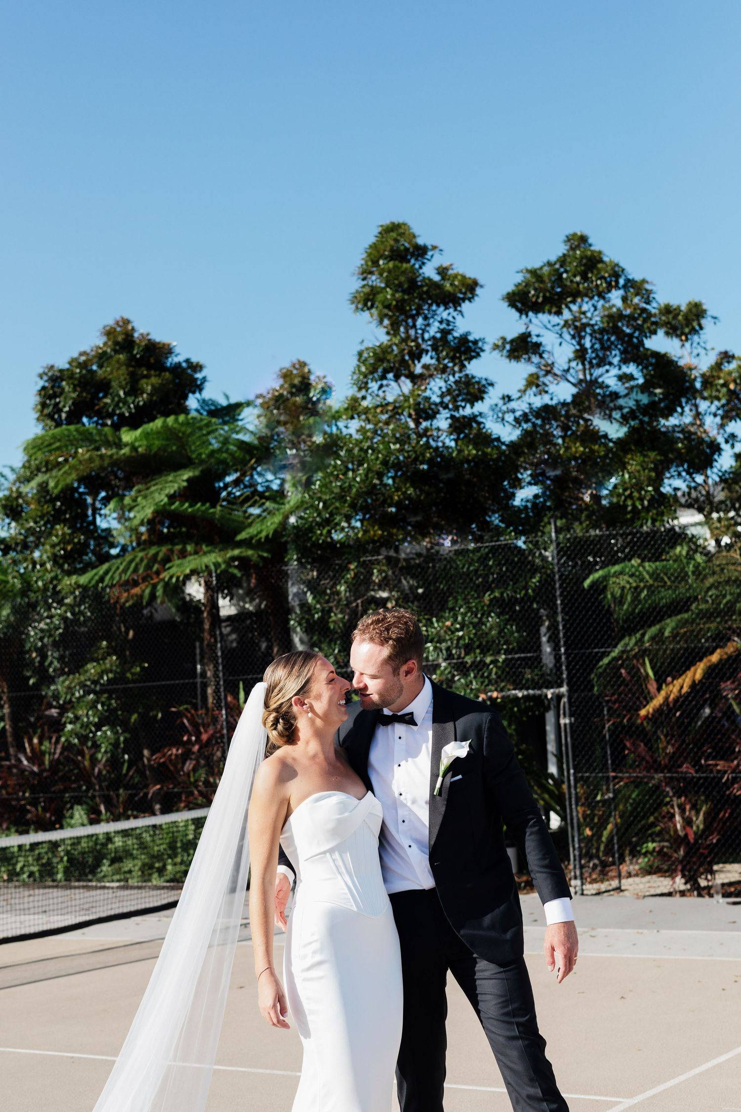 Happy bride and groom holding hands walking down outdoor aisle after wedding ceremony, palm trees in background.