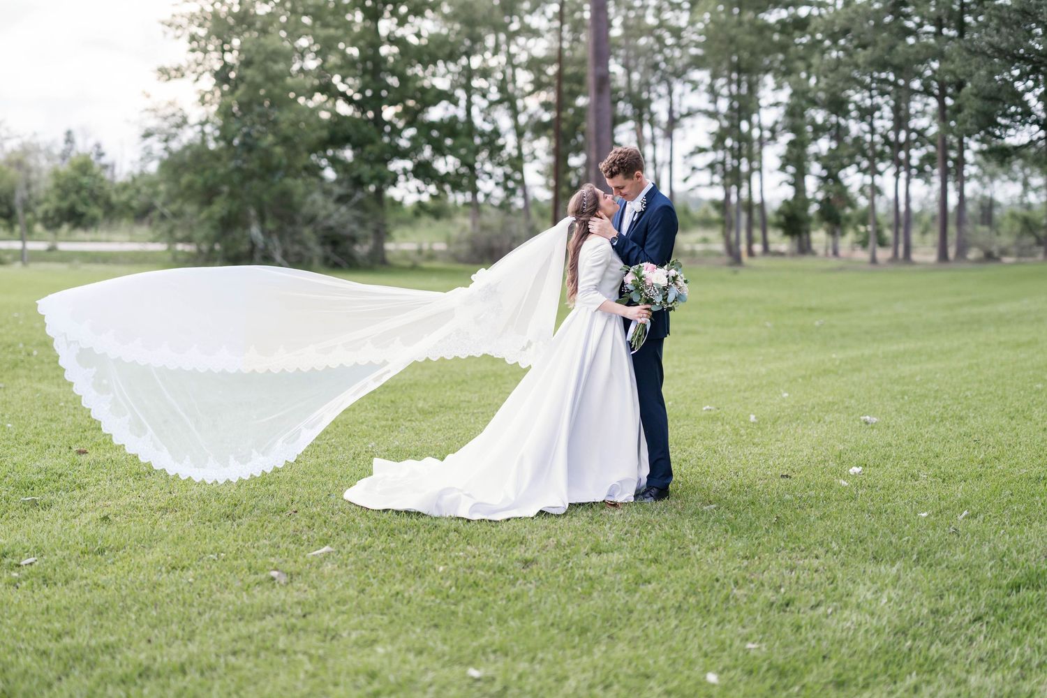 modest bride and groom kiss as veil blows in the wind