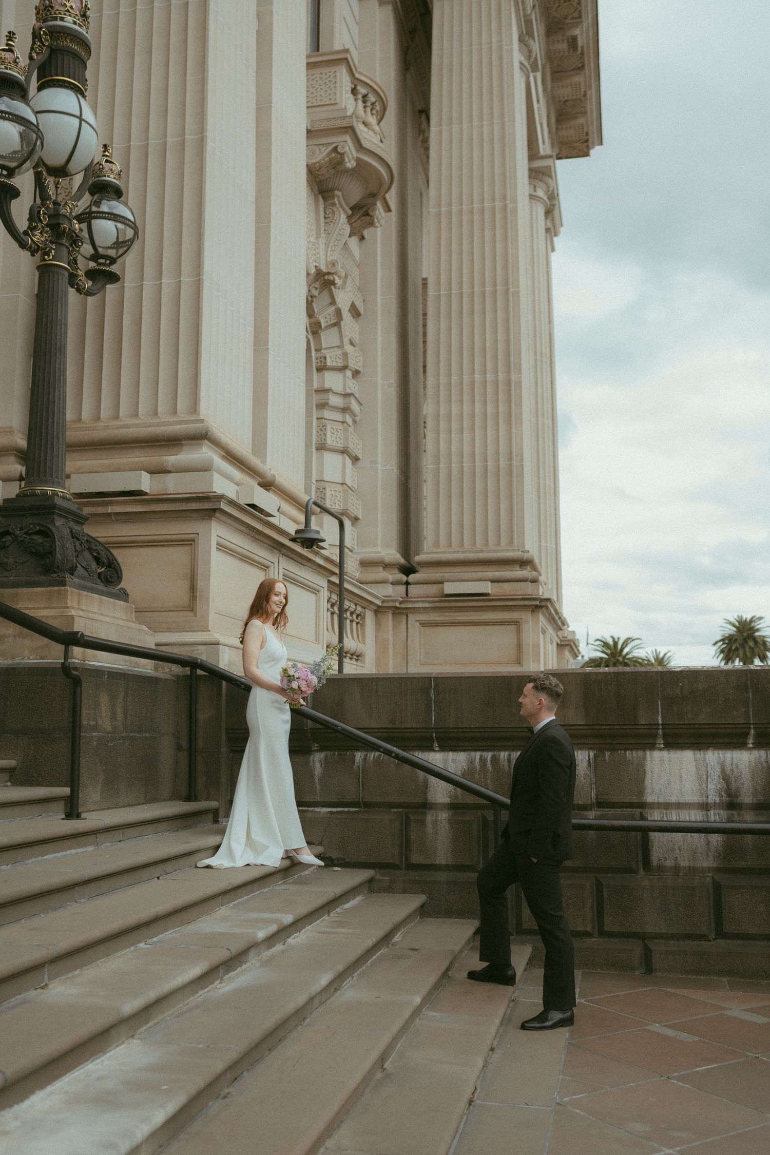 Bride and groom share a romantic first look on grand stone steps of a classical building on their wedding day.