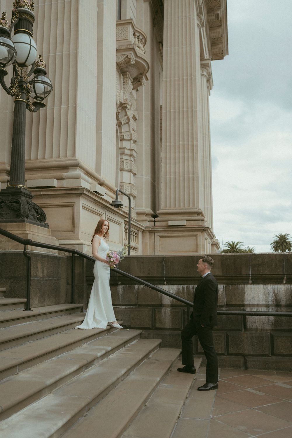 Bride and groom share a romantic first look on grand stone steps of a classical building on their wedding day.
