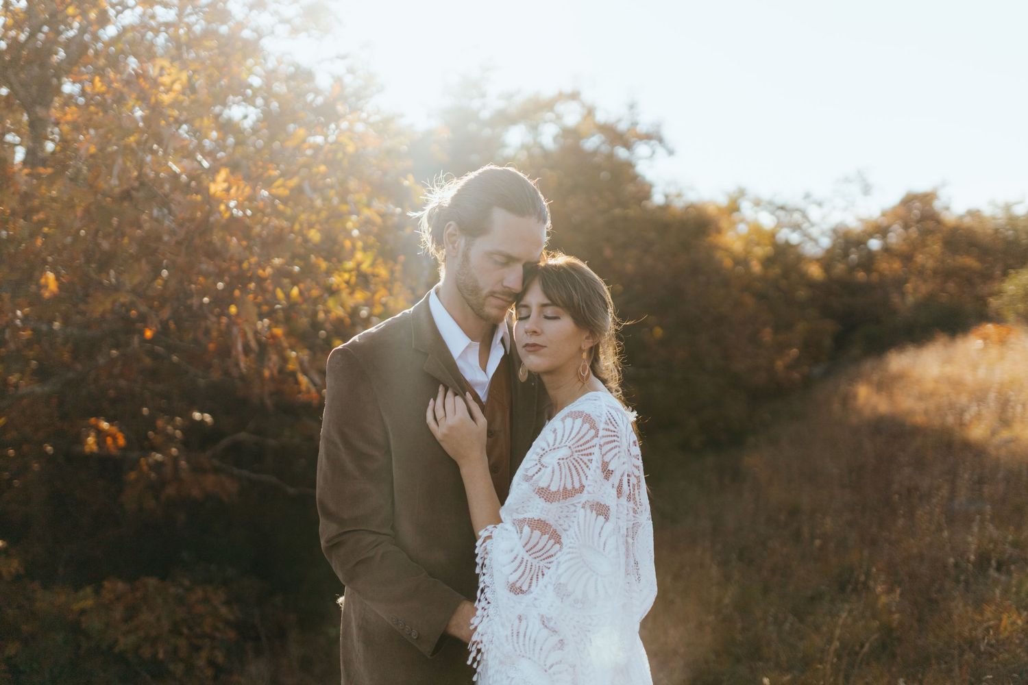 A romantic couple embraces in a golden autumn field during sunset creating a dreamy outdoor portrait.