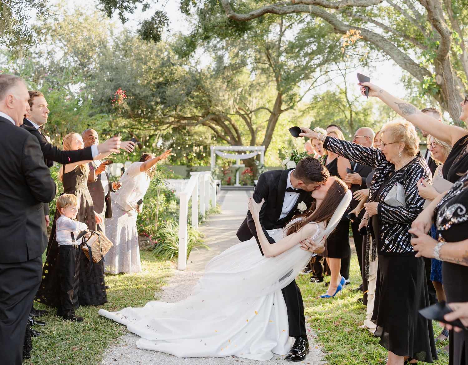 White horse-drawn Cinderella carriage on green lawn under large oak tree at elegant outdoor wedding.