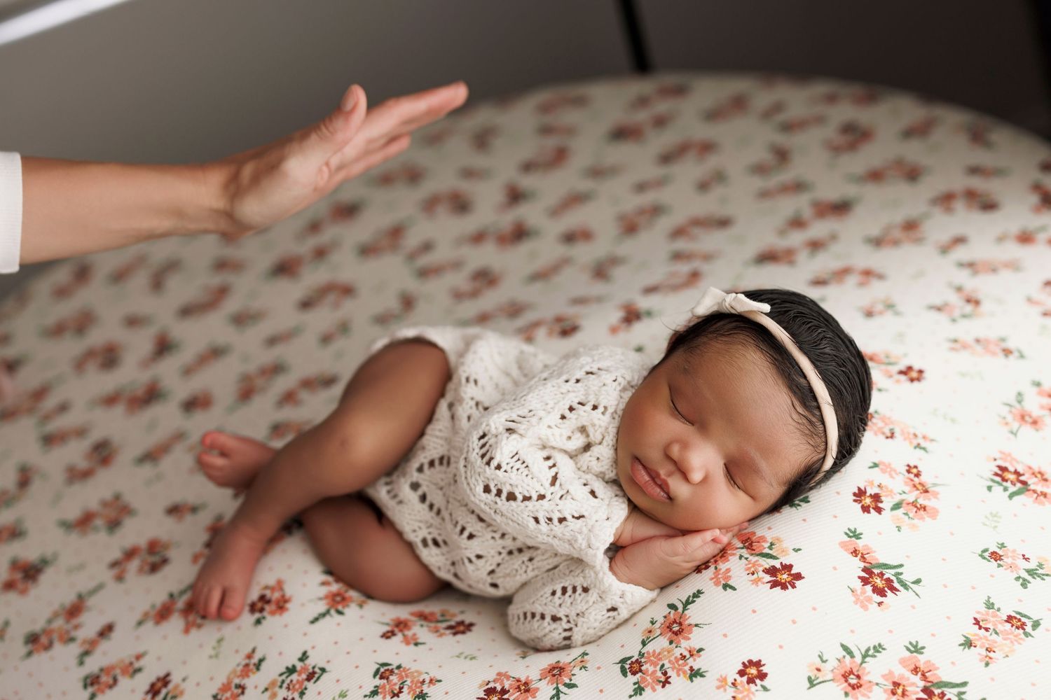 Peaceful newborn baby sleeping on floral blanket wearing white lace outfit and dark headband.
